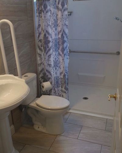 A bathroom featuring a sink, toilet, shower with a curtain and handrail.