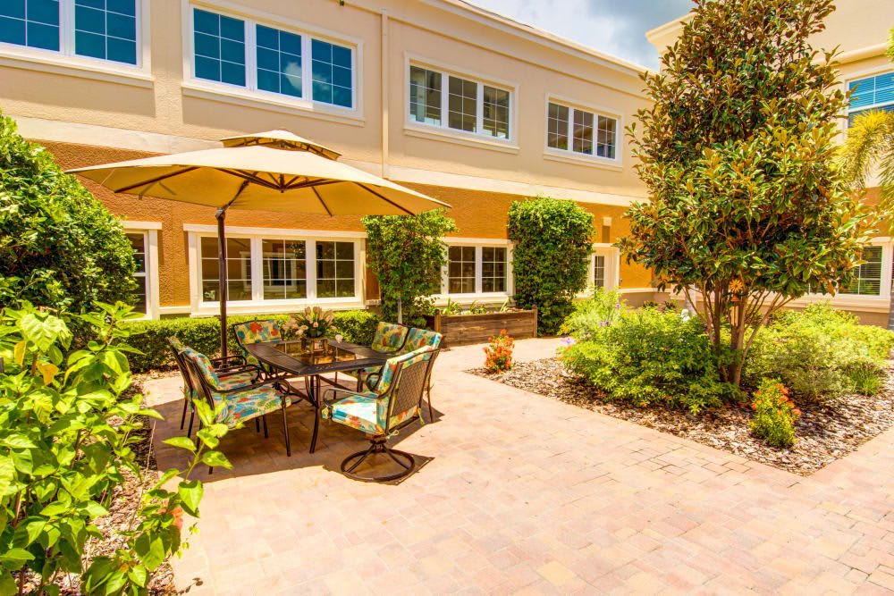 A sunny outdoor patio with seating and an umbrella in a landscaped garden area.