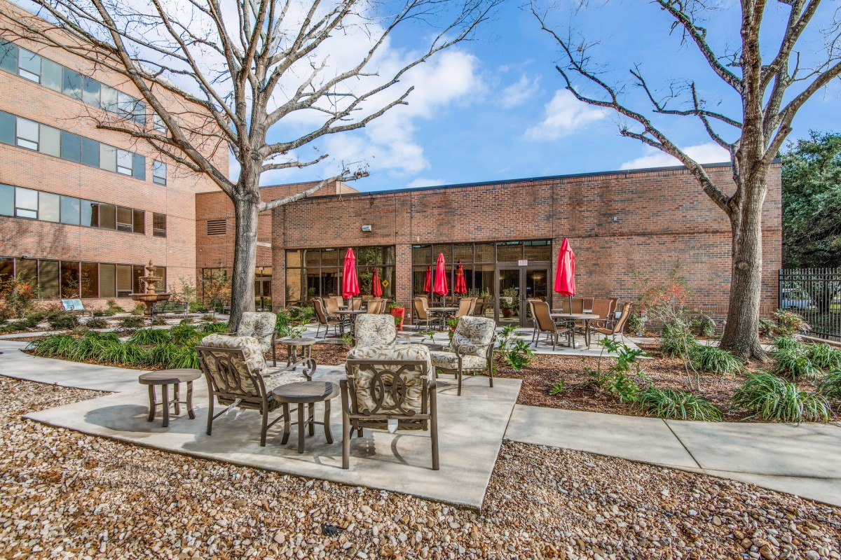A cozy outdoor patio area with comfortable seating and red umbrellas, set against a brick building.