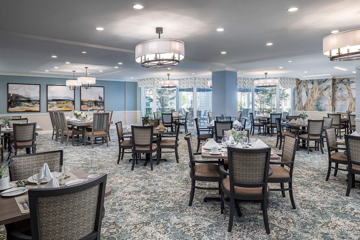 A spacious dining room with elegant decor, featuring multiple tables and chairs, chandeliers, and a carpeted floor.