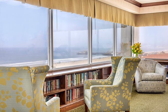 A cozy reading nook with comfortable chairs and bookshelves overlooking a scenic view through large windows.