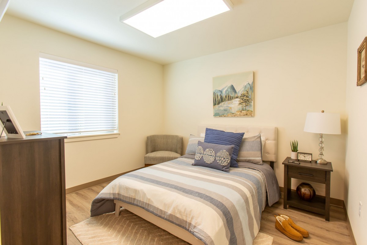 A cozy bedroom interior with a neatly made bed, artwork on the wall, and soft natural lighting.