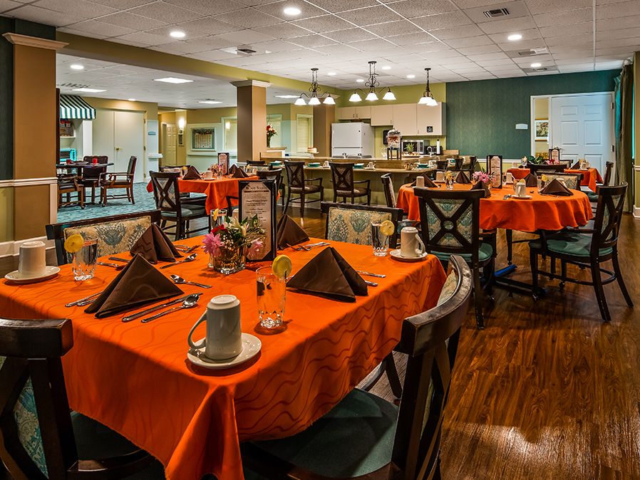 A well-decorated dining area with tables set for service, featuring orange tablecloths and neatly arranged utensils.