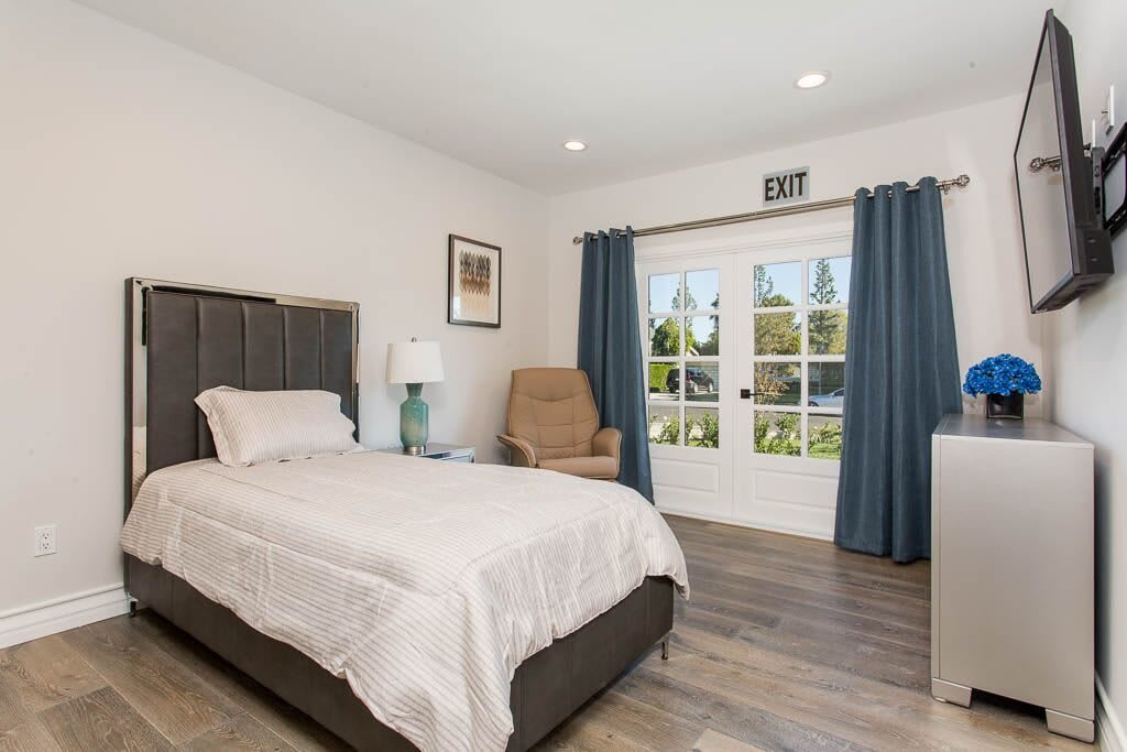 A cozy bedroom with a single bed, armchair, and large window.