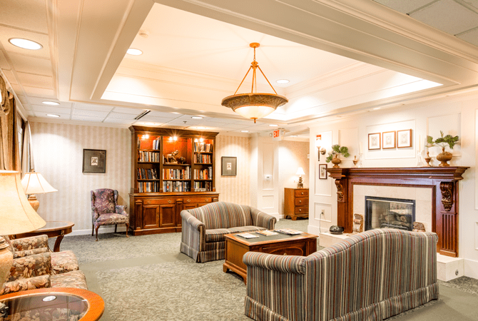 A cozy living room featuring a striped sofa set, a wooden bookshelf filled with books, and an inviting fireplace.