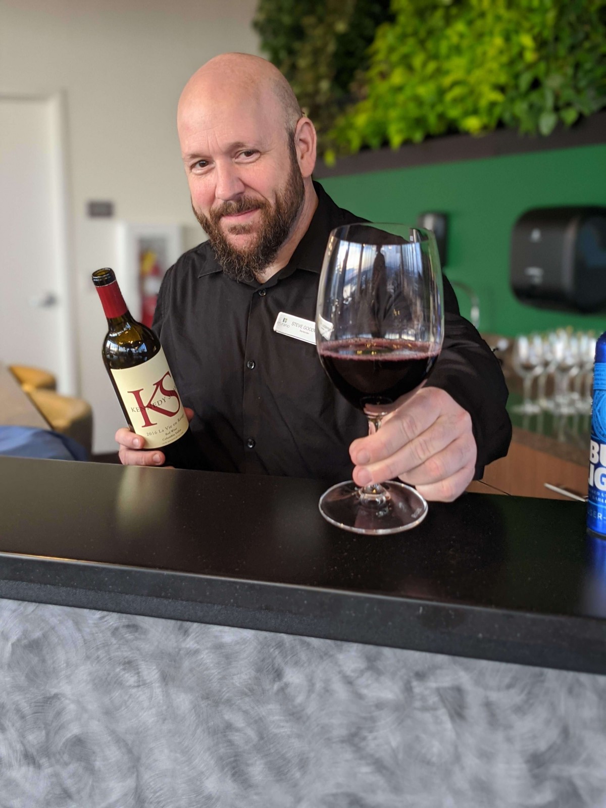 A bartender presenting a glass of red wine at the bar.