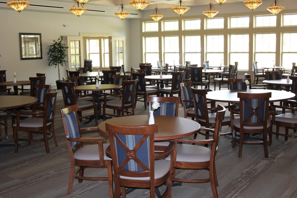 An empty dining room with wooden tables and chairs, large windows, and ceiling fans.