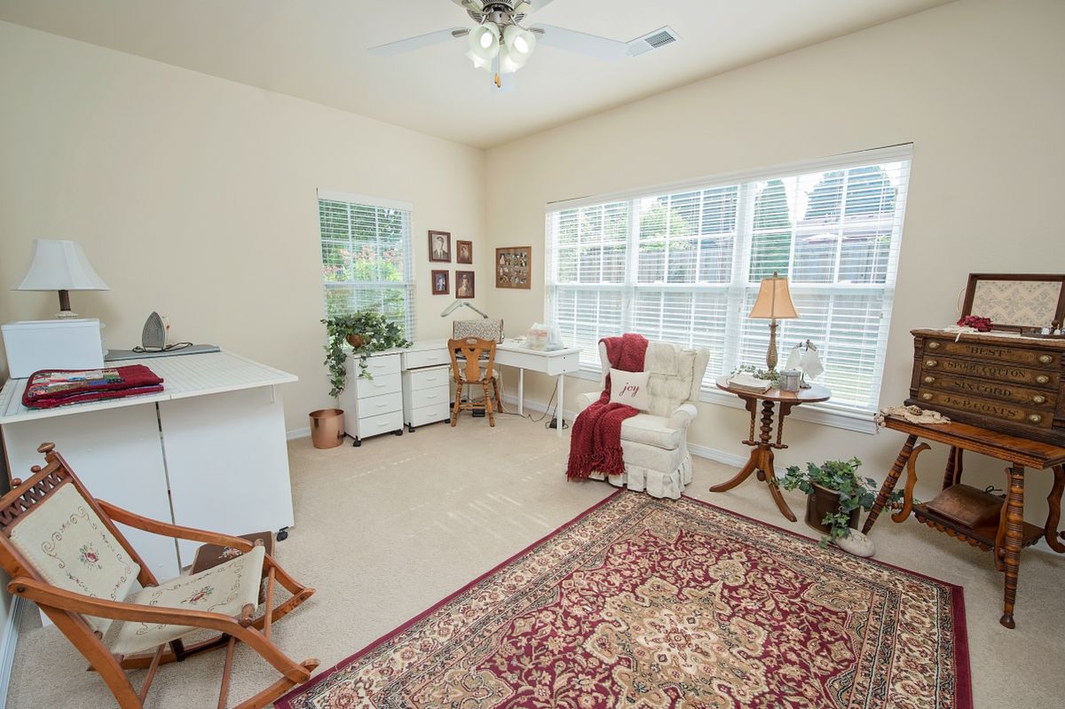 A cozy home office setup in a sunlit room with large windows, featuring a desk, comfortable chair, and decorative elements.