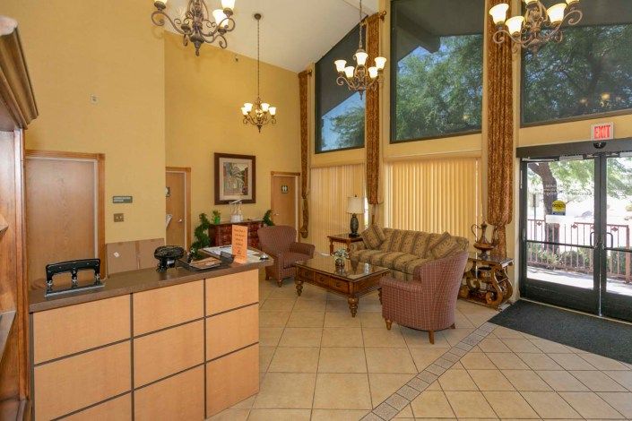 A hotel lobby with a reception desk, elegant chandeliers, and comfortable seating area.