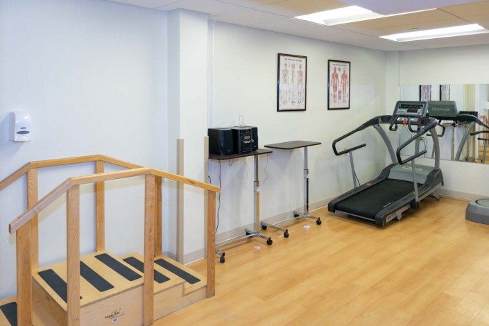 A physical therapy room equipped with a treadmill and a set of stairs for rehabilitation exercises.