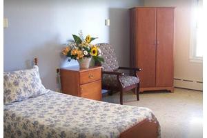 A cozy bedroom with a bed, wardrobe, armchair, and a bedside table adorned with a vase of flowers.