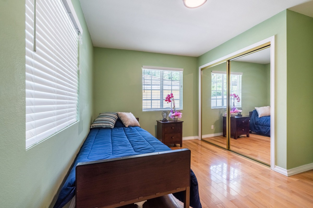 A cozy bedroom featuring a single bed with a blue comforter, green walls, and mirrored closet doors.