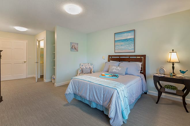 A cozy bedroom with a neatly made bed, soft lighting, and beach-themed artwork on the wall.