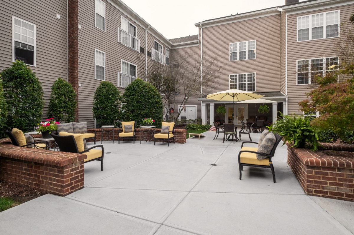 A cozy courtyard featuring outdoor seating with comfortable chairs and landscaping, set against the backdrop of apartment buildings.