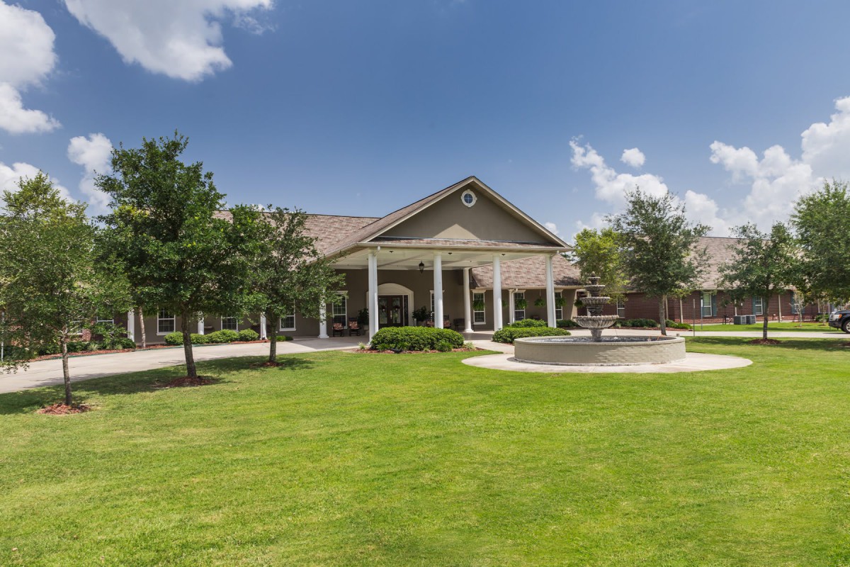 A spacious building with a well-maintained lawn and surrounding trees under a clear blue sky.