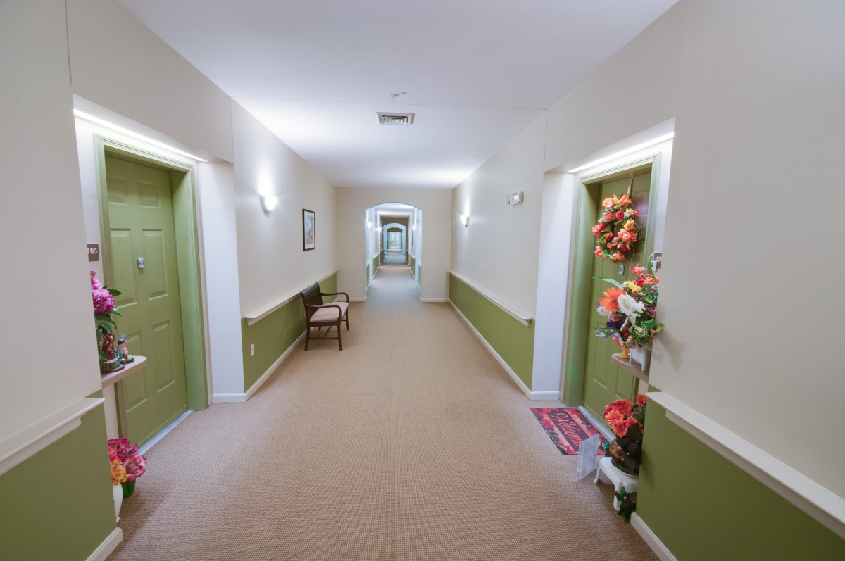 A brightly lit hallway with doors on either side, some decorated with flowers.