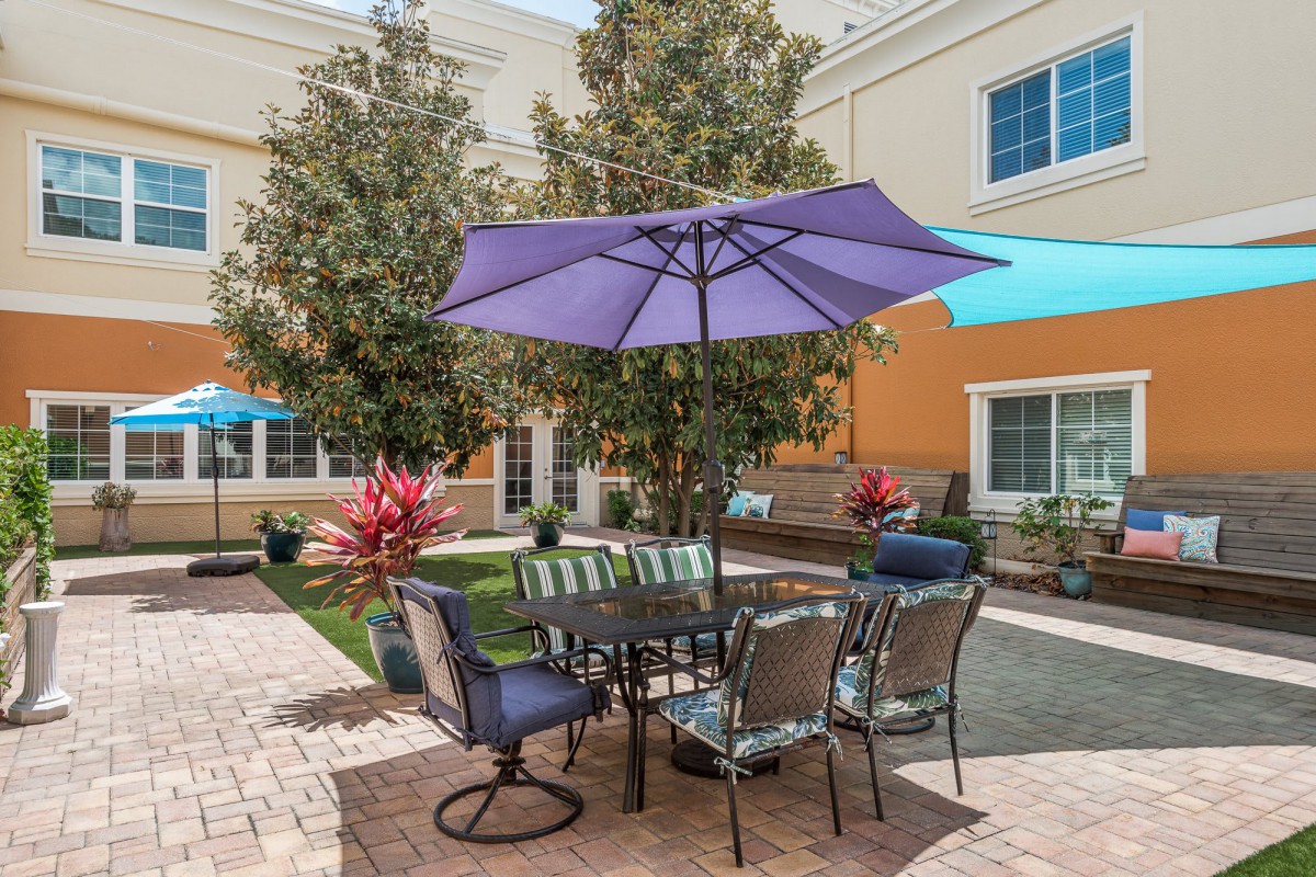 A well-furnished patio area with an umbrella, surrounded by a garden setting.