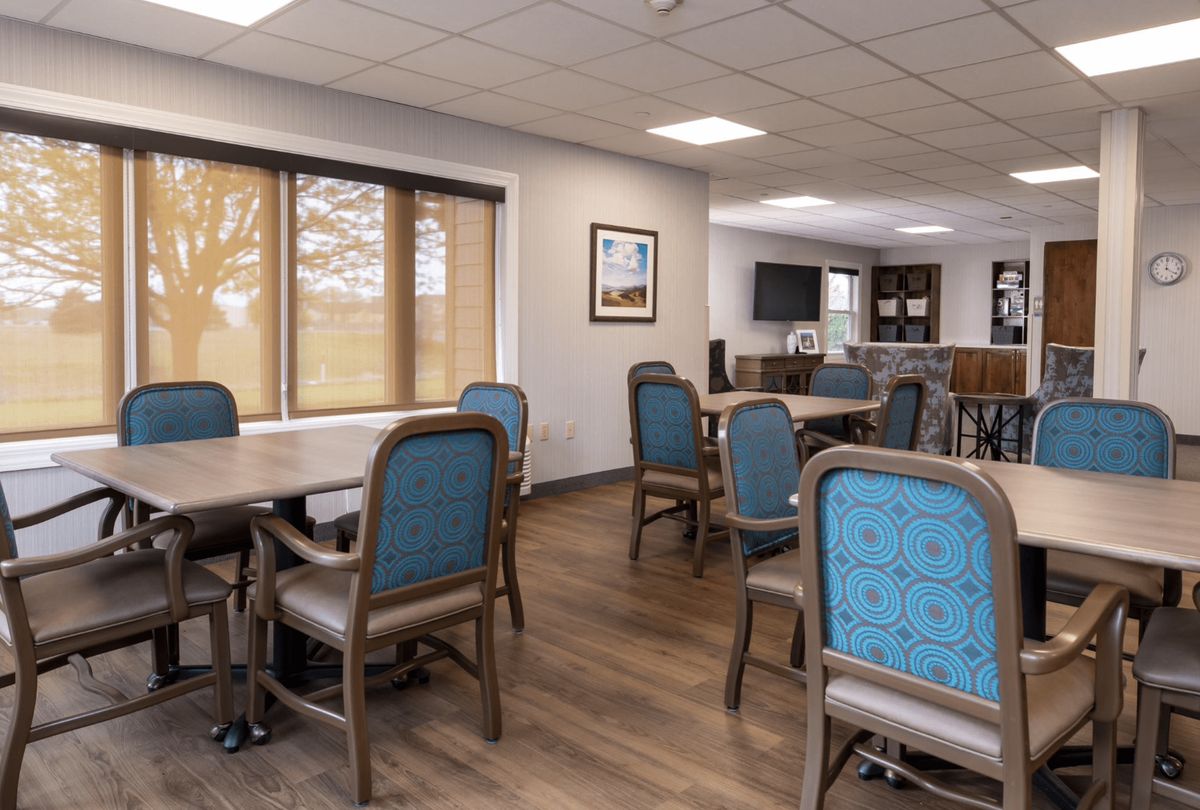 A spacious dining room with tables and chairs, featuring large windows and a wooden floor.