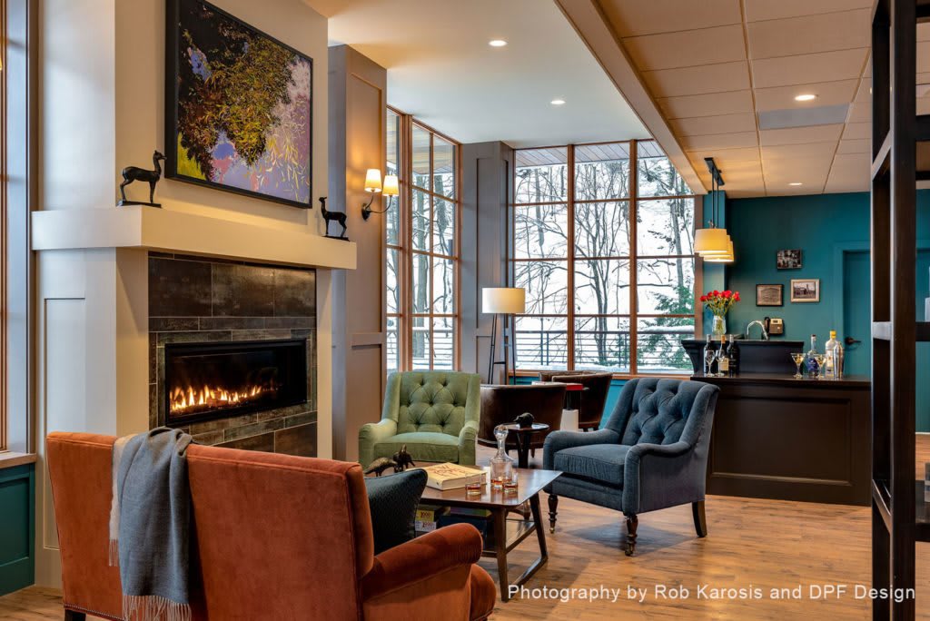 A cozy living room with a fireplace, armchairs, and large windows.
