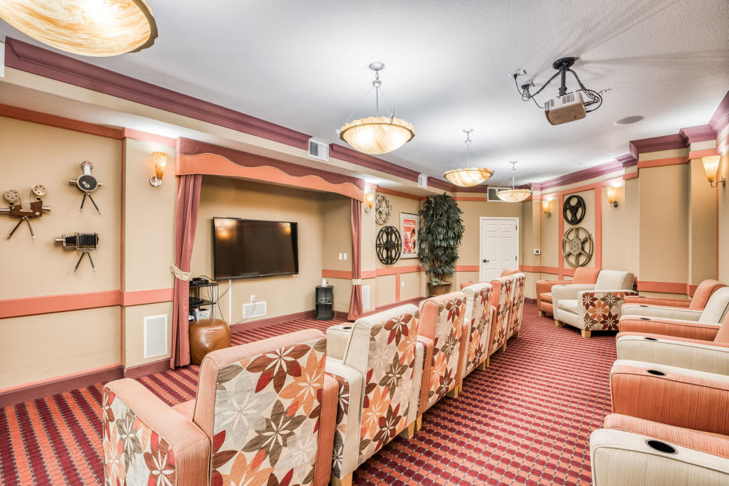 A cozy theater room with floral-patterned seating, a television mounted on the wall, and soft decorative lighting.