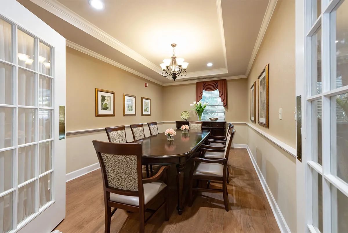 A neatly arranged dining room with a long table, surrounded by chairs and illuminated by a chandelier.