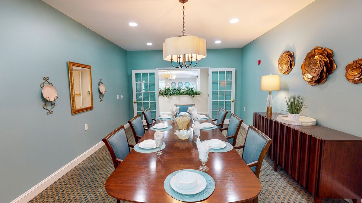 An elegantly designed dining room featuring a large wooden table set for a meal, with a chandelier overhead and blue painted walls.
