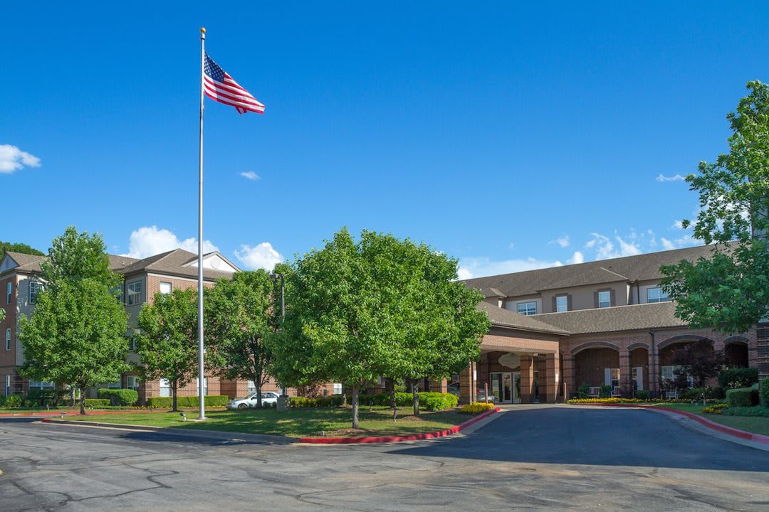 A building with an American flag in front, surrounded by trees and a parking lot under a clear blue sky.