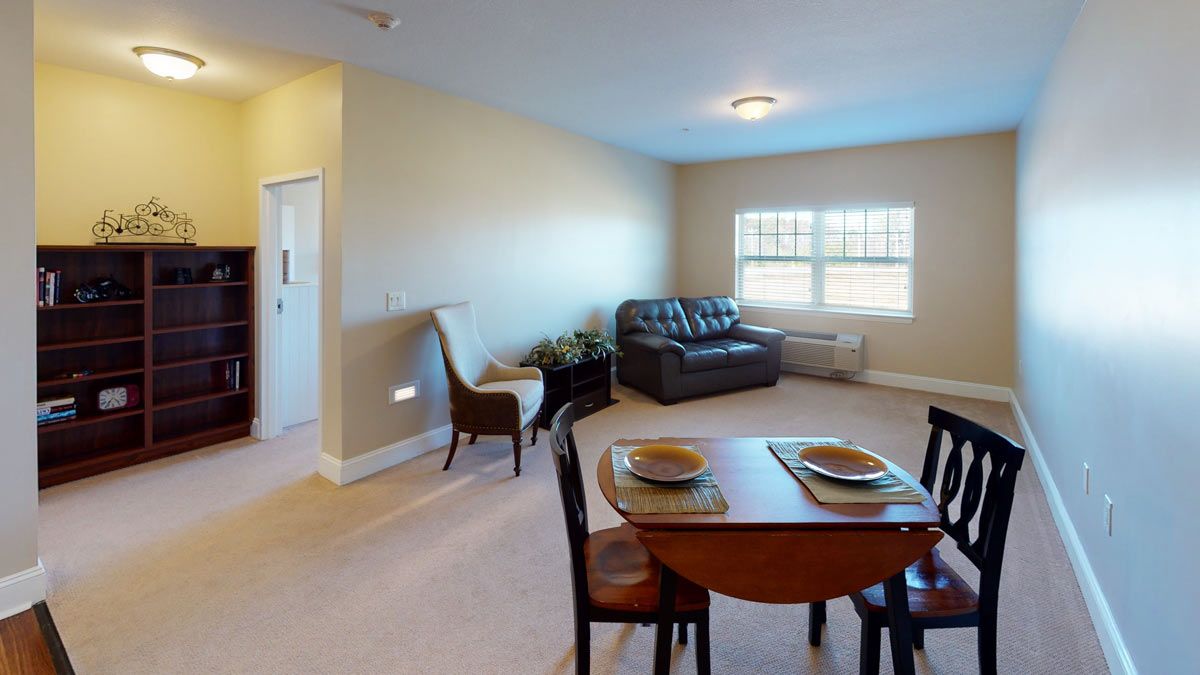 A cozy living and dining space featuring a small dining table, chairs, and a sofa by the window.