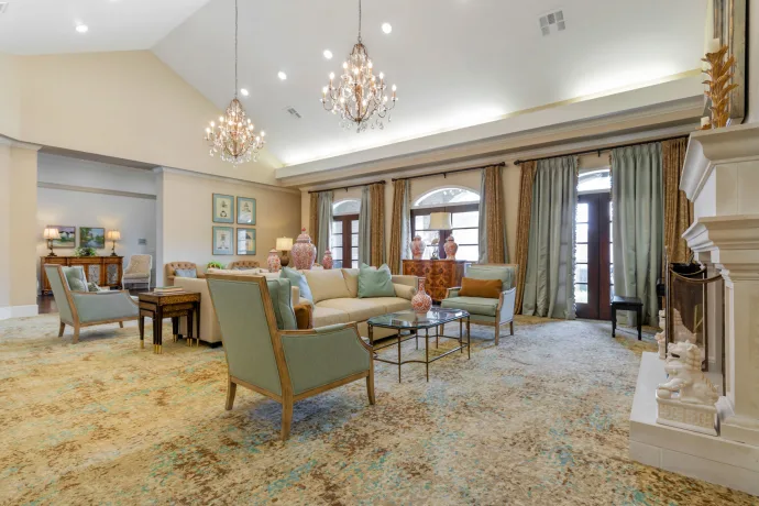 A spacious and elegantly designed living room featuring comfortable seating, ornate chandeliers, and large windows with curtains.