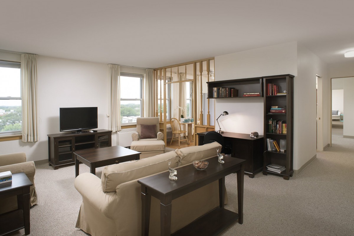 A modern living room with a cozy sofa, coffee table, bookshelf, desk, and television.