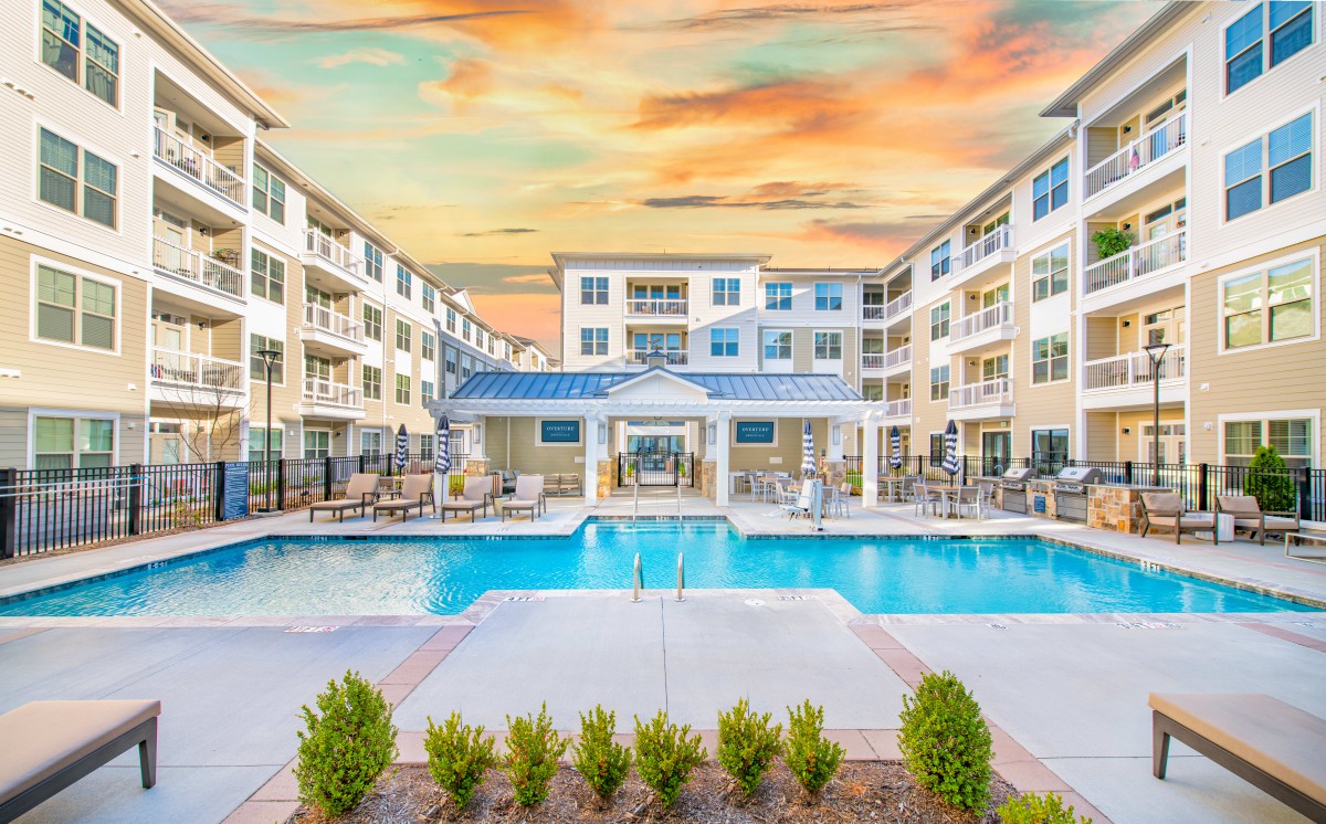 A modern apartment complex with a central swimming pool at sunset.