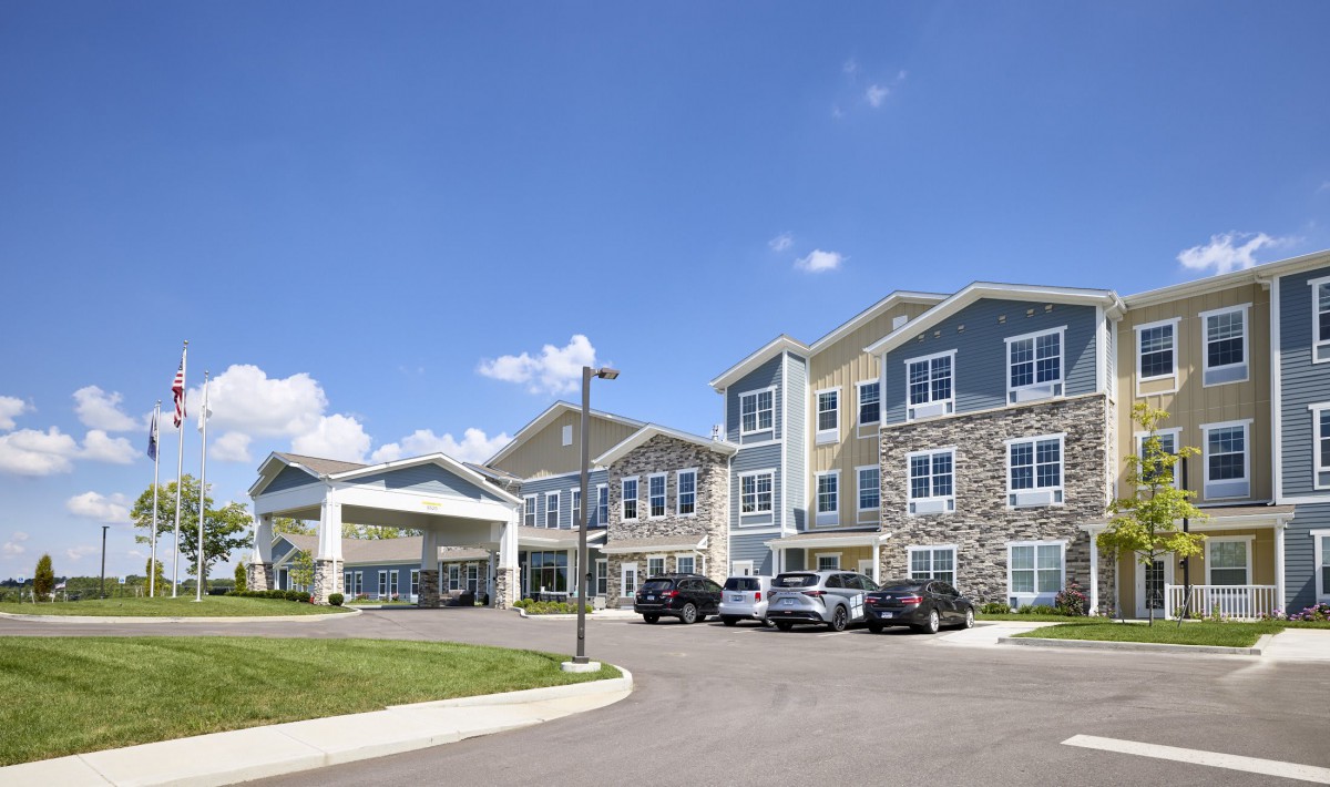 A modern residential building with a parking lot and cars under a clear blue sky.
