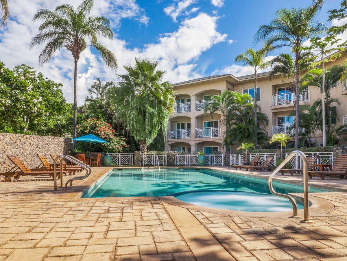A tropical resort with a swimming pool surrounded by palm trees under a clear blue sky.