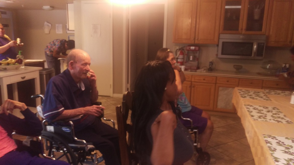 A family gathering in a living room with an elderly man in a wheelchair and others seated nearby.