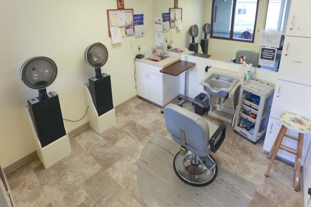 An interior view of a barbershop with chairs, mirrors, and hair drying equipment.