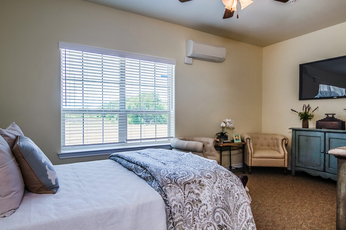 A cozy bedroom with a bed, comfortable seating, and a large window letting in natural light.
