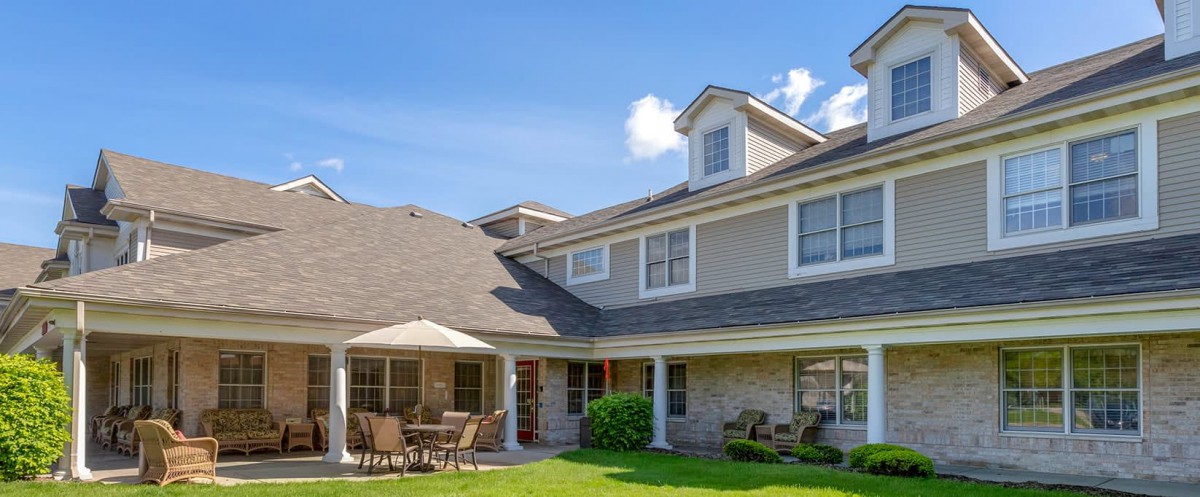A sunny day view of a spacious two-story house with a well-maintained lawn and patio furniture.