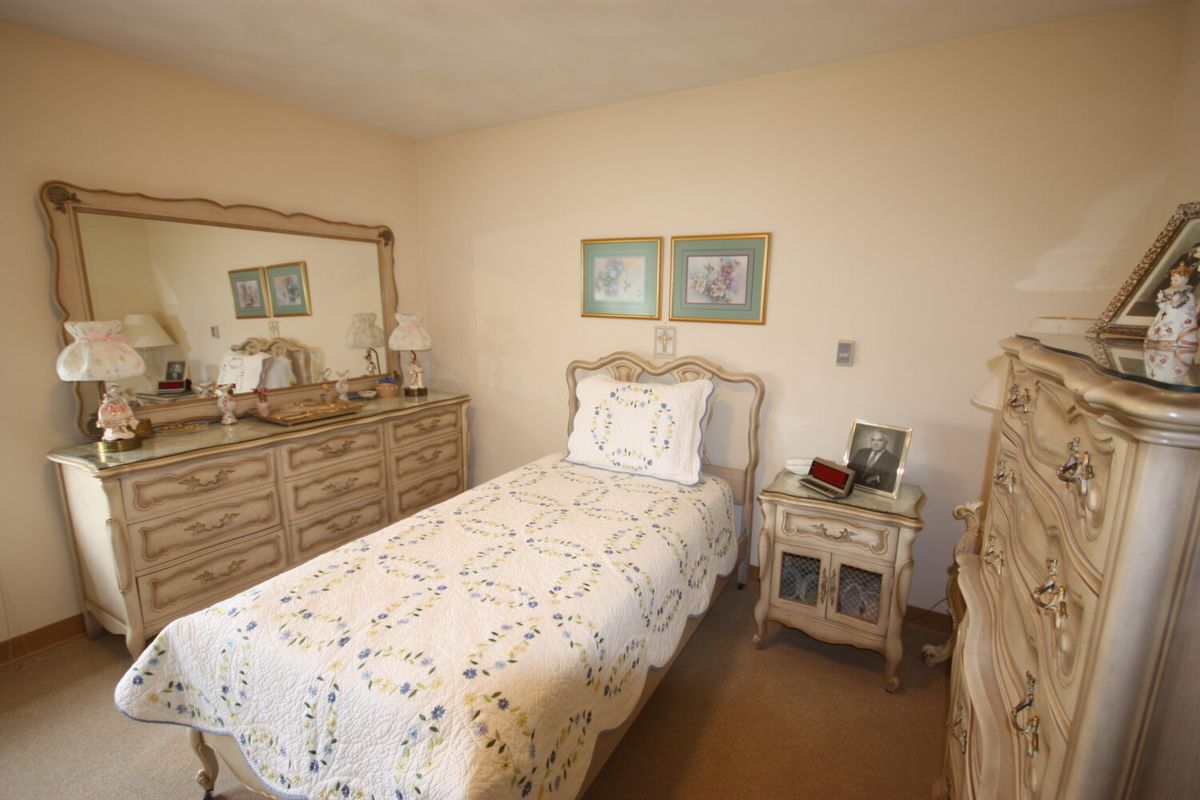 A neatly arranged bedroom with a single bed, dresser, and mirror in neutral tones.
