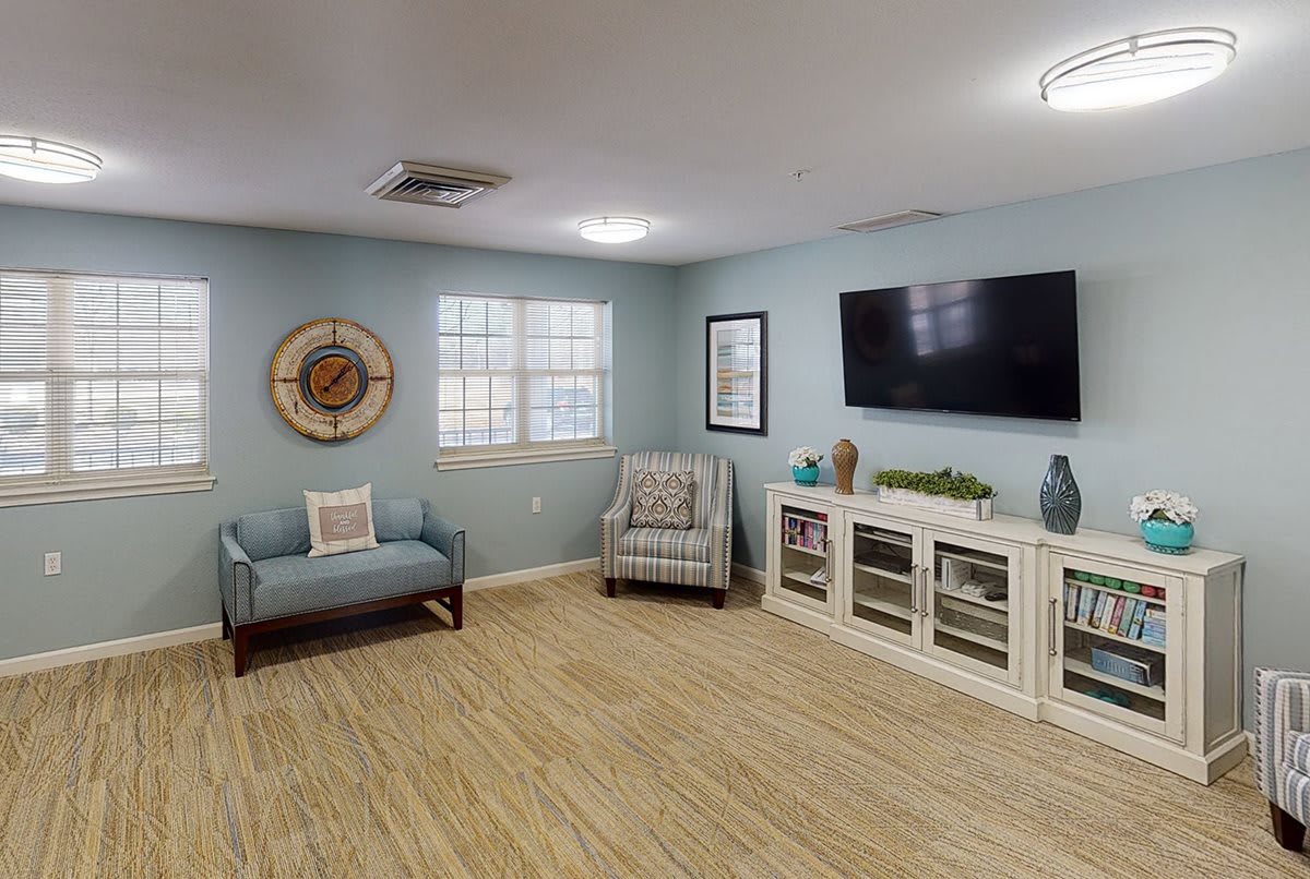 A modern living room with light blue walls, featuring a TV, comfortable chairs, and decorative accents.