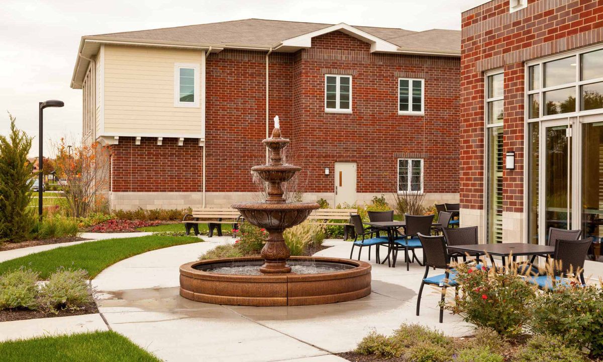 A tranquil courtyard with a central fountain surrounded by outdoor seating and a brick building backdrop.