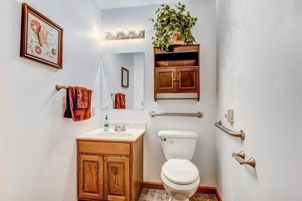 A compact bathroom with a sink, toilet, mirror, and wooden cabinets, complemented by red towels and an indoor plant.