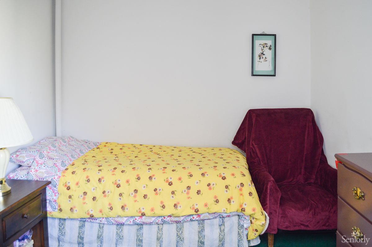 A minimalist bedroom with a bed covered by a yellow blanket and a burgundy chair.