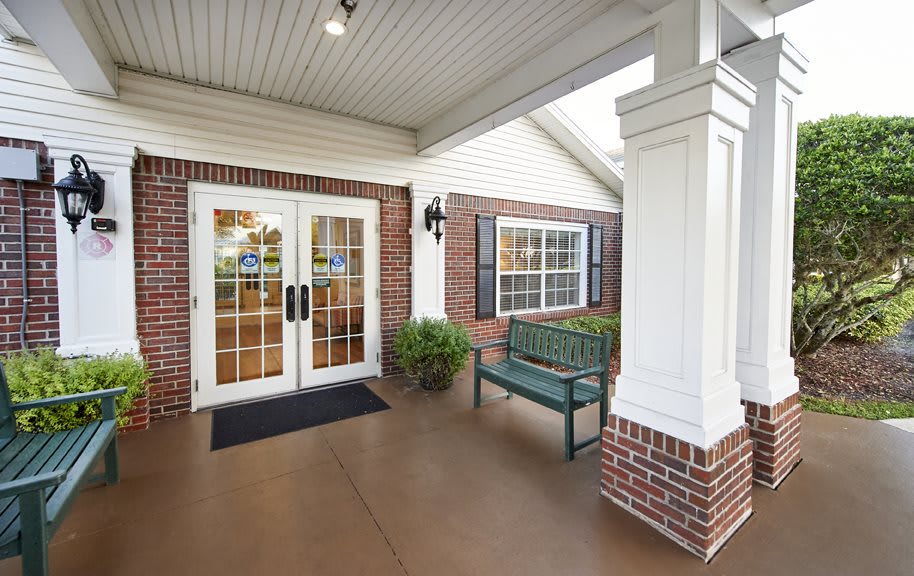 A welcoming building entrance with double glass doors, a bench, and decorative plants.