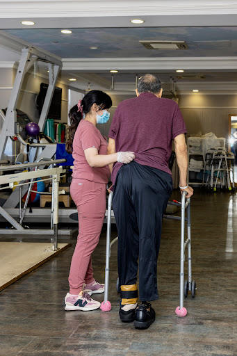 A healthcare professional assists an elderly patient during a rehabilitation session.