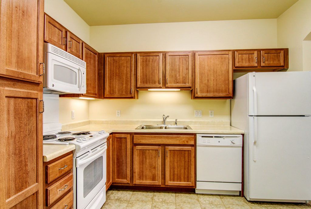 A kitchen with wooden cabinets featuring a microwave, oven, refrigerator, and dishwasher.