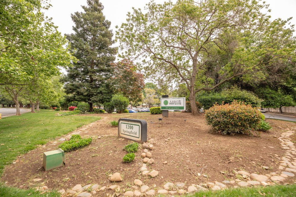 A landscaped park area with signs and various trees providing greenery.