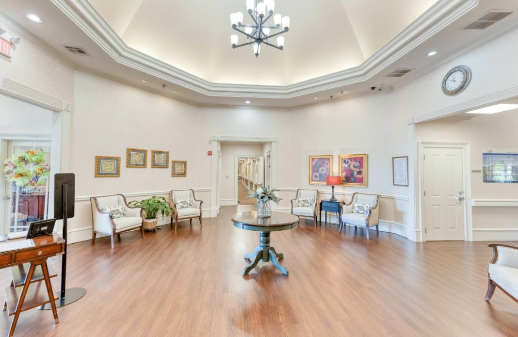 A spacious lobby area with elegant decor, featuring a central round table, comfortable chairs, and a large chandelier.