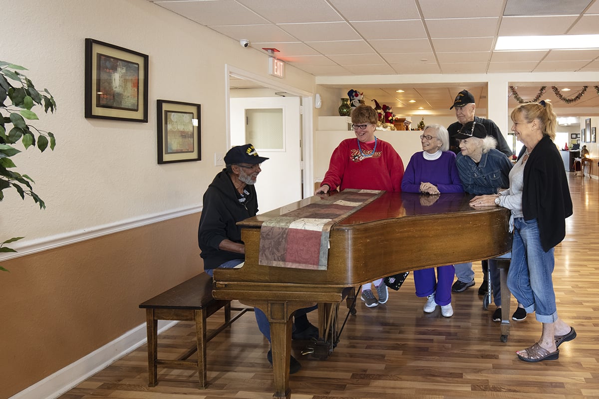 A group of people gathered around a piano to enjoy a musical performance indoors.