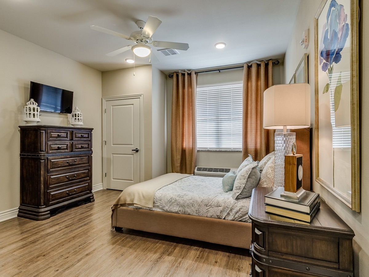 A cozy bedroom with a neatly made bed, a dresser, and warm lighting.
