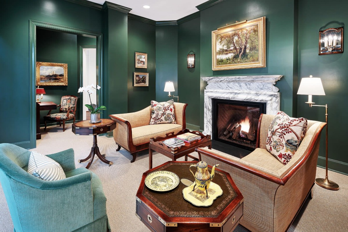 A cozy living room with green walls, traditional furniture, and a marble fireplace.